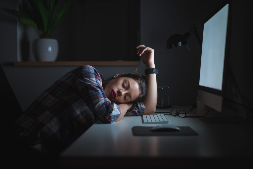 Shift worker asleep at her desk in front of her computer with the monitor still on